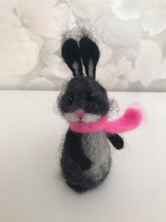 Felted rabbit toy with a pink scarf on a white background